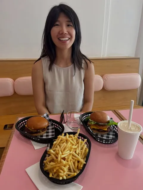 A guest at a pink Pearls booth with burgers, fries and a shake