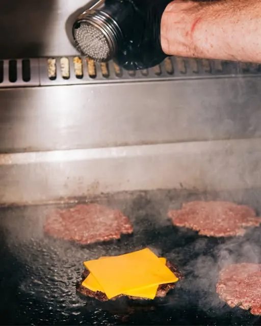 A Pearls cook seasoning fresh smash patties on the grill