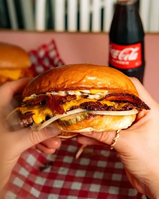 Double bacon cheeseburger held up in front of a bottle of Coke